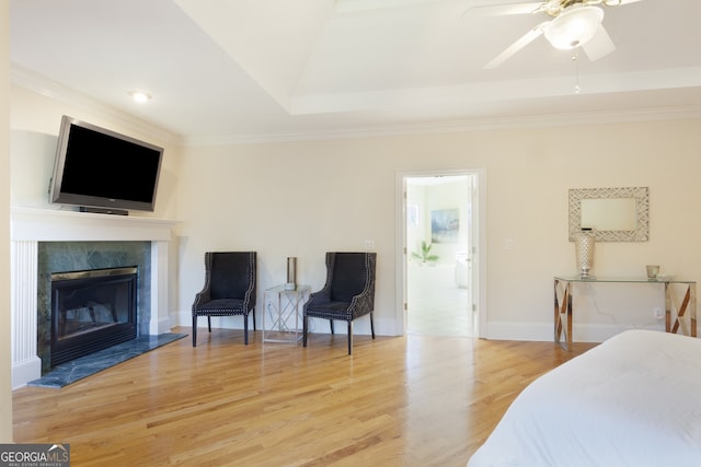 bedroom featuring ceiling fan, ornamental molding, a fireplace, a tray ceiling, and wood-type flooring