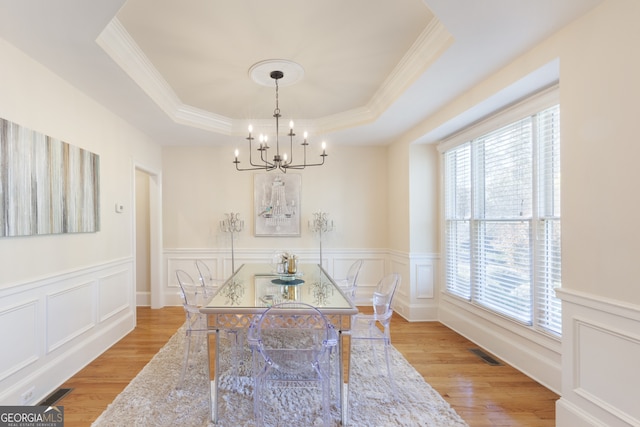 dining space with a chandelier, ornamental molding, light hardwood / wood-style flooring, and a tray ceiling