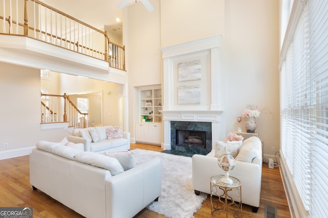 living room featuring built in shelves, a fireplace, hardwood / wood-style floors, and a high ceiling