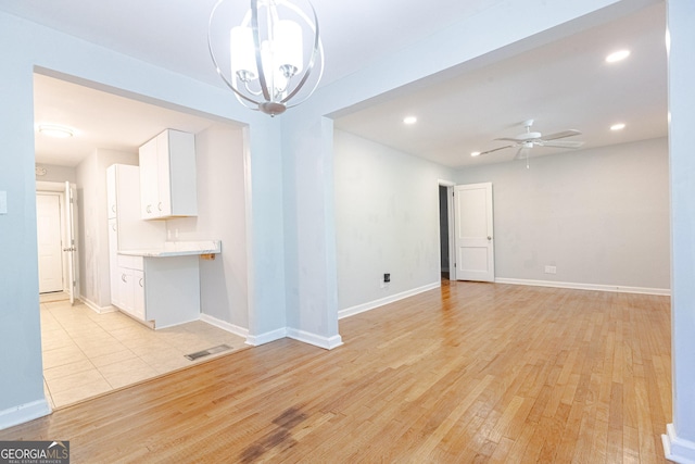 spare room featuring ceiling fan with notable chandelier and light hardwood / wood-style flooring