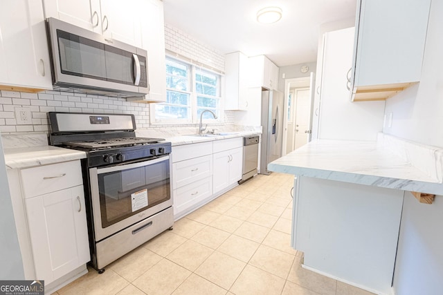 kitchen with appliances with stainless steel finishes, backsplash, sink, light tile patterned floors, and white cabinets