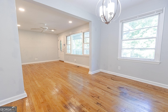 empty room with ceiling fan with notable chandelier and light wood-type flooring