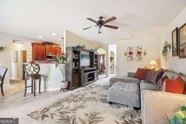 living room featuring arched walkways, ceiling fan, baseboards, recessed lighting, and light colored carpet
