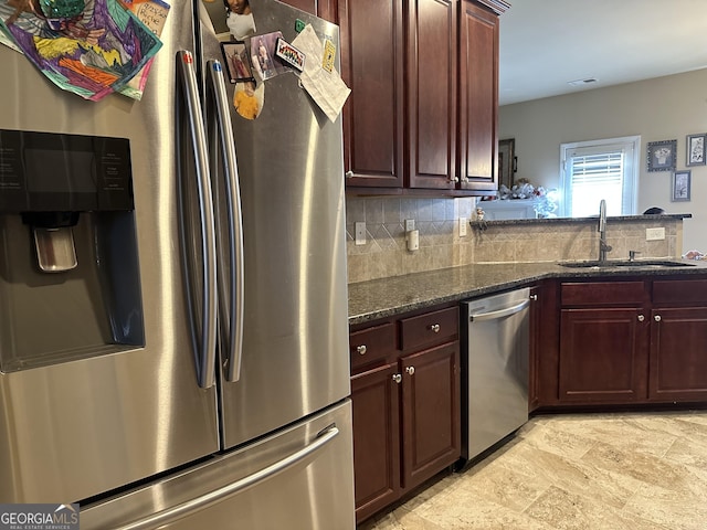 kitchen with appliances with stainless steel finishes, a sink, tasteful backsplash, dark stone counters, and light stone finish flooring