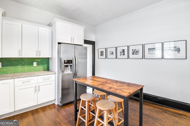 kitchen featuring dark hardwood / wood-style flooring, white cabinetry, stainless steel fridge with ice dispenser, light stone countertops, and decorative backsplash