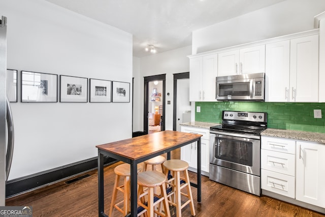 kitchen with light stone countertops, white cabinets, dark wood-type flooring, stainless steel appliances, and backsplash