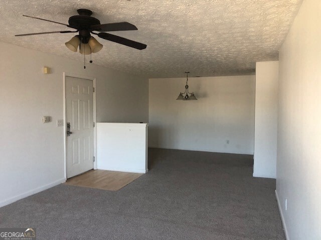 unfurnished room with ceiling fan, dark carpet, and a textured ceiling