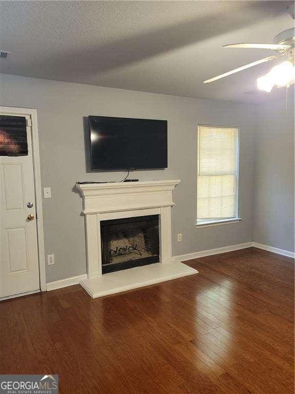 unfurnished living room with a textured ceiling, ceiling fan, and dark wood-type flooring