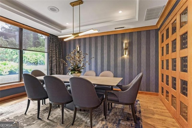 dining area with a tray ceiling, wood-type flooring, and ornamental molding