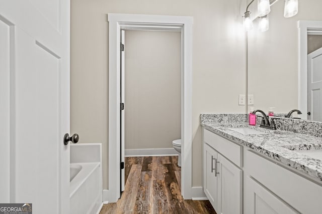 bathroom featuring a bath, hardwood / wood-style floors, vanity, and toilet