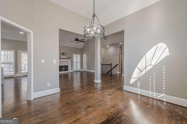 unfurnished dining area featuring dark wood-type flooring, high vaulted ceiling, a healthy amount of sunlight, and ceiling fan with notable chandelier