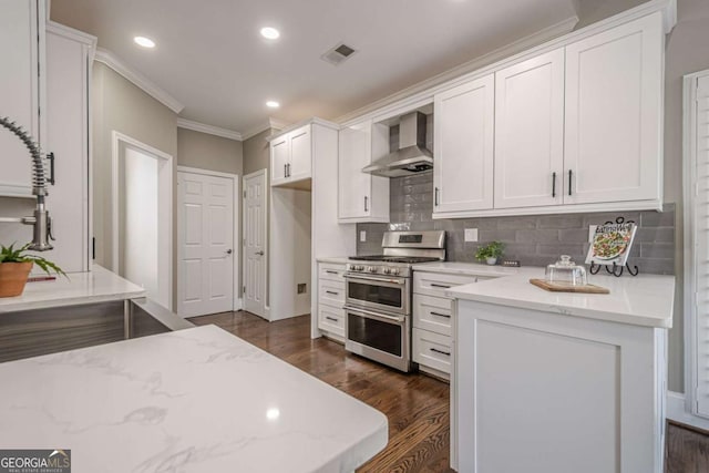 kitchen featuring backsplash, range with two ovens, wall chimney exhaust hood, light stone counters, and white cabinetry