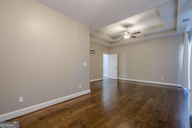 unfurnished room with a raised ceiling, ceiling fan, dark wood-type flooring, and a textured ceiling