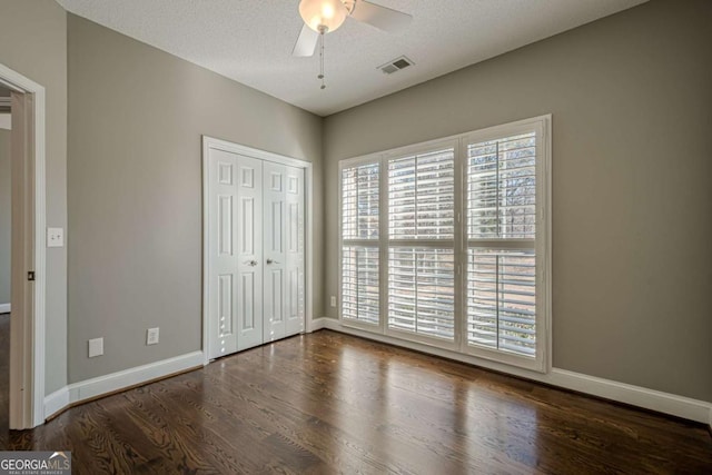 unfurnished bedroom featuring ceiling fan, dark hardwood / wood-style floors, a textured ceiling, and a closet