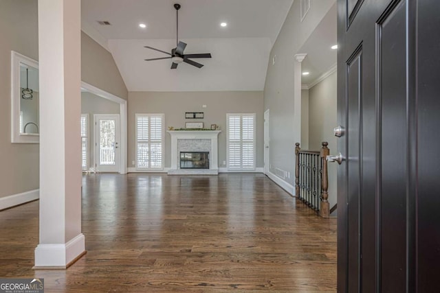 unfurnished living room with ceiling fan, dark wood-type flooring, a stone fireplace, high vaulted ceiling, and crown molding