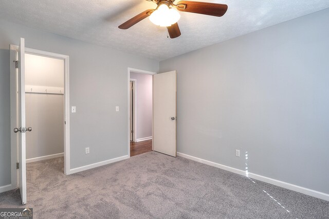 unfurnished bedroom with ceiling fan, a spacious closet, light colored carpet, a textured ceiling, and a closet