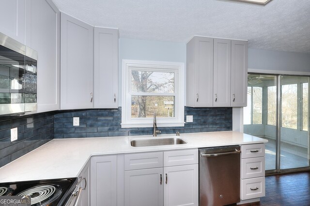 kitchen with backsplash, dark wood-type flooring, a stone fireplace, gray cabinets, and appliances with stainless steel finishes