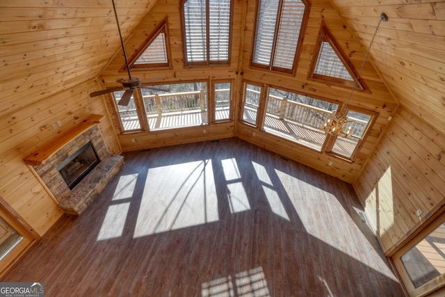 unfurnished living room with dark hardwood / wood-style flooring, ceiling fan with notable chandelier, vaulted ceiling, wooden walls, and a fireplace