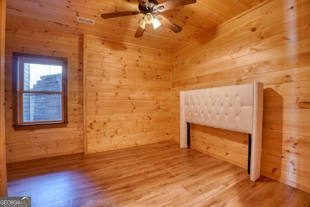 unfurnished bedroom with light wood-type flooring, wooden ceiling, ceiling fan, and wooden walls