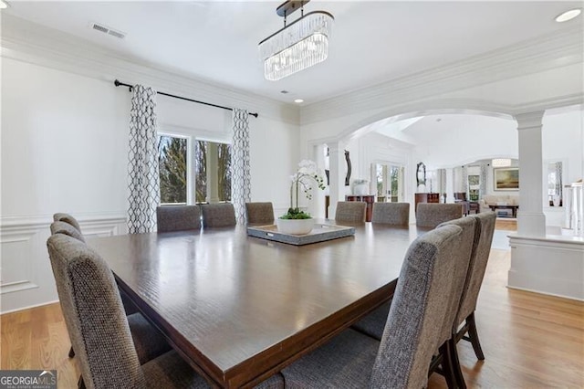 dining space with ornamental molding, ornate columns, a notable chandelier, and light wood-type flooring