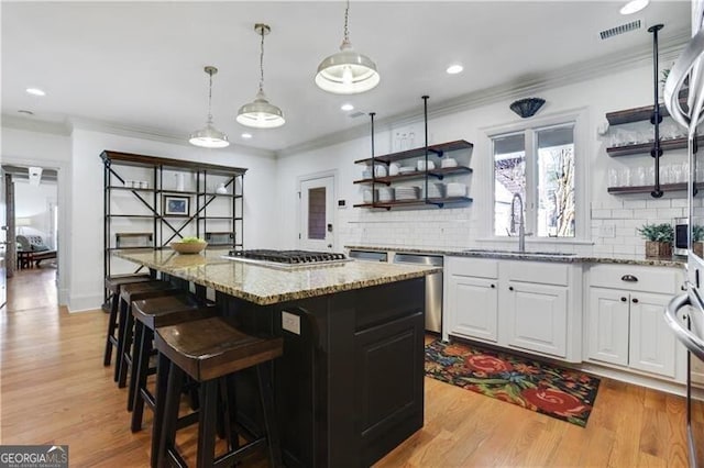 kitchen with white cabinets, appliances with stainless steel finishes, a kitchen island, sink, and light wood-type flooring