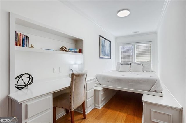 bedroom featuring ornamental molding, built in desk, and light wood-type flooring