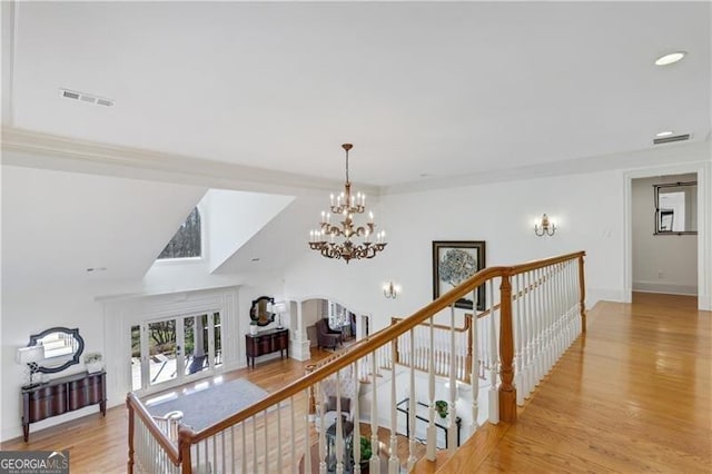 staircase with ornamental molding, hardwood / wood-style flooring, and a notable chandelier