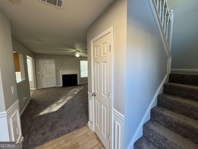 staircase with ceiling fan, plenty of natural light, wood-type flooring, and a textured ceiling