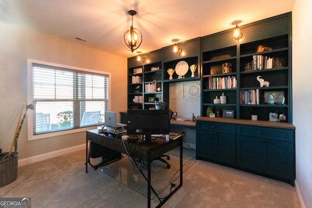 office with built in shelves, carpet, and a notable chandelier