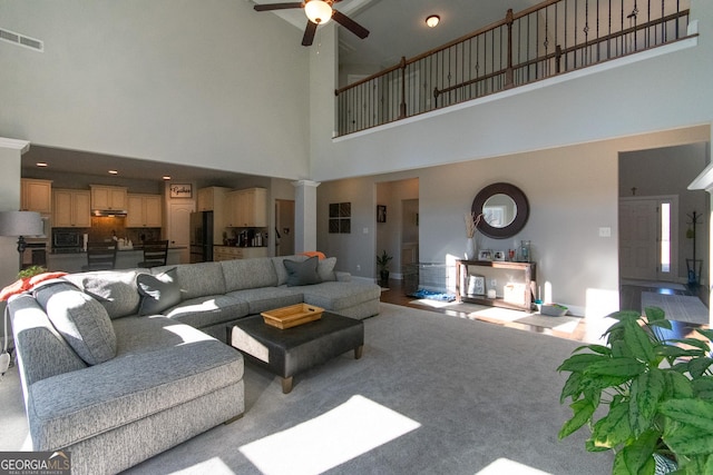 living room with ceiling fan, light carpet, and a high ceiling