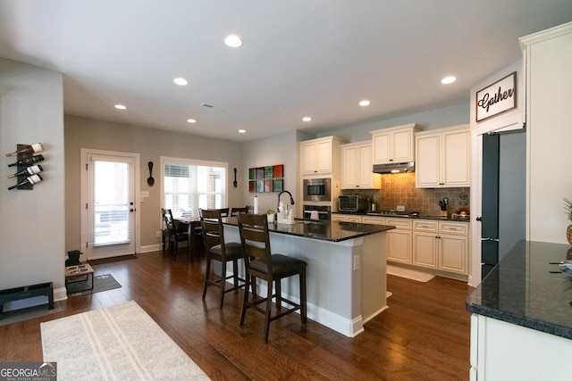 kitchen featuring sink, dark hardwood / wood-style floors, dark stone countertops, an island with sink, and stainless steel appliances