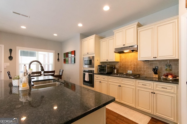 kitchen featuring dark stone counters, cream cabinets, sink, light hardwood / wood-style flooring, and appliances with stainless steel finishes