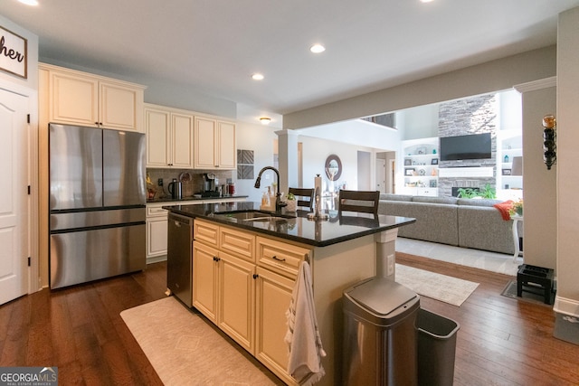 kitchen with sink, dark wood-type flooring, black dishwasher, stainless steel fridge, and a kitchen island with sink