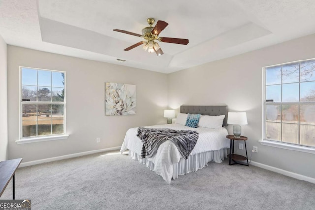 bedroom with light carpet, a tray ceiling, and ceiling fan