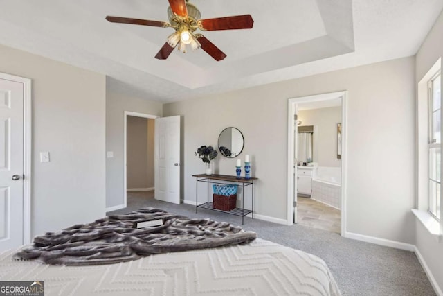 bedroom with ensuite bath, light colored carpet, a raised ceiling, and ceiling fan