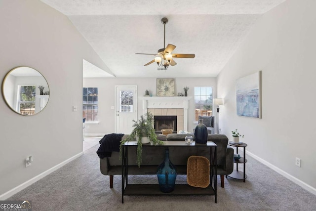 living room featuring carpet, a tile fireplace, vaulted ceiling, ceiling fan, and a textured ceiling