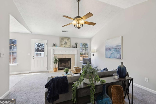 carpeted living room featuring a textured ceiling, vaulted ceiling, ceiling fan, a tile fireplace, and plenty of natural light