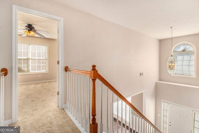 hallway with a healthy amount of sunlight, a chandelier, light carpet, and a textured ceiling