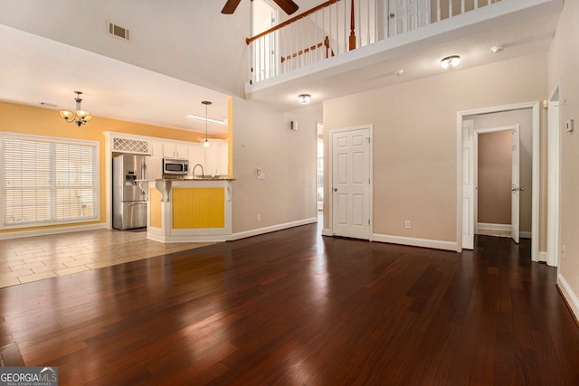 unfurnished living room featuring ceiling fan with notable chandelier, dark wood-type flooring, and a towering ceiling