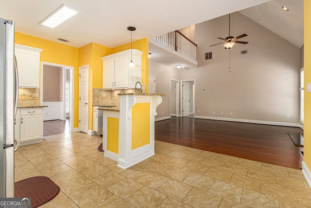 kitchen with white cabinetry, light stone countertops, kitchen peninsula, and stainless steel refrigerator