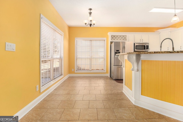 kitchen with a breakfast bar area, white cabinetry, stainless steel appliances, light stone counters, and decorative light fixtures