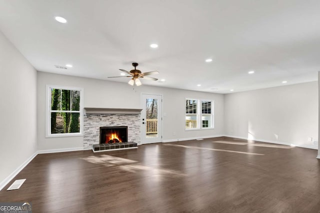 unfurnished living room featuring a stone fireplace, ceiling fan, and dark hardwood / wood-style flooring