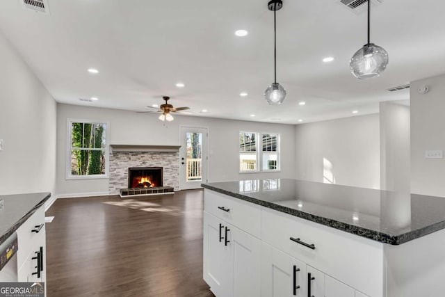 kitchen featuring a fireplace, white cabinetry, hanging light fixtures, and dark stone countertops