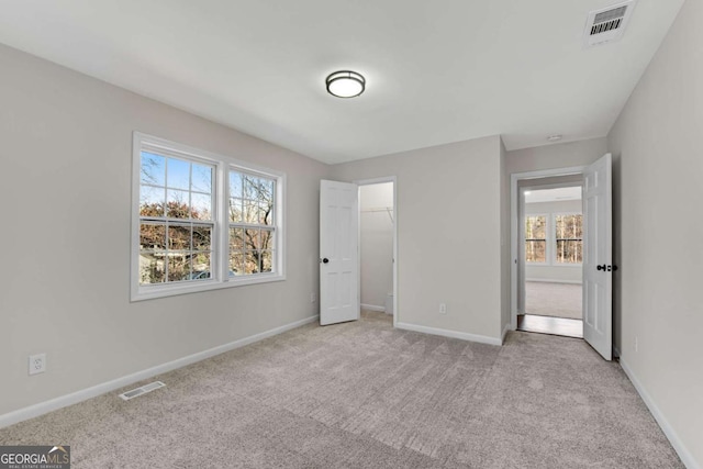 unfurnished bedroom featuring a closet, light colored carpet, a spacious closet, and multiple windows