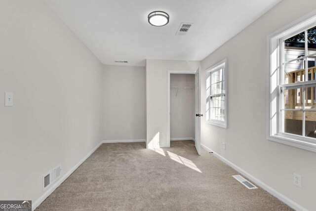 unfurnished bedroom with multiple windows, light carpet, and a closet