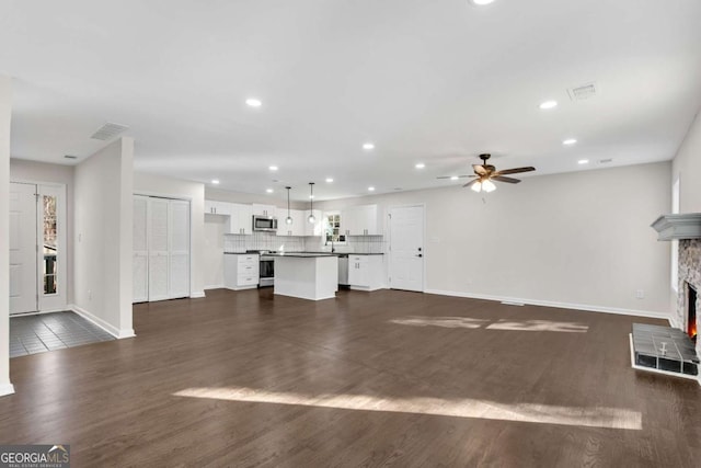 unfurnished living room with ceiling fan, a stone fireplace, and dark wood-type flooring