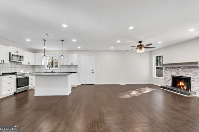 kitchen featuring ceiling fan, a stone fireplace, pendant lighting, white cabinets, and appliances with stainless steel finishes