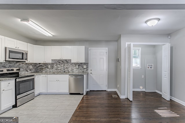 kitchen with stainless steel appliances, light stone counters, decorative backsplash, white cabinets, and sink