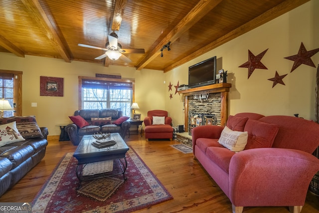 living room featuring ceiling fan, beam ceiling, a stone fireplace, and wood-type flooring