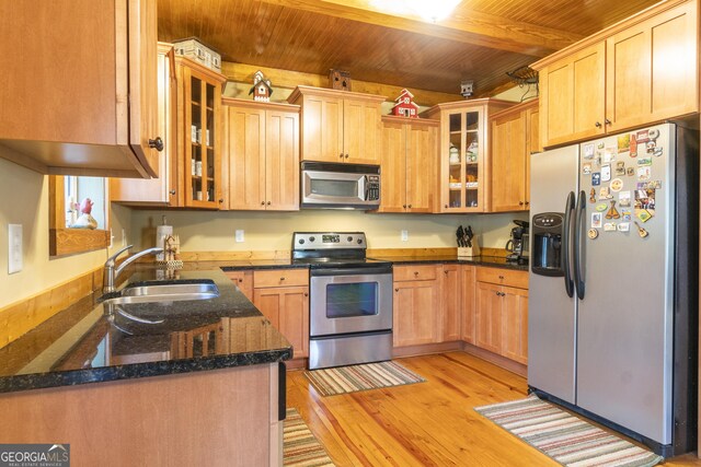 kitchen featuring light wood-type flooring, stainless steel appliances, sink, dark stone countertops, and beamed ceiling